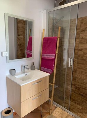 Bathroom features a sink, mirror, and vanity with two drawers, as well as a shower with glass doors and a wooden panel design.