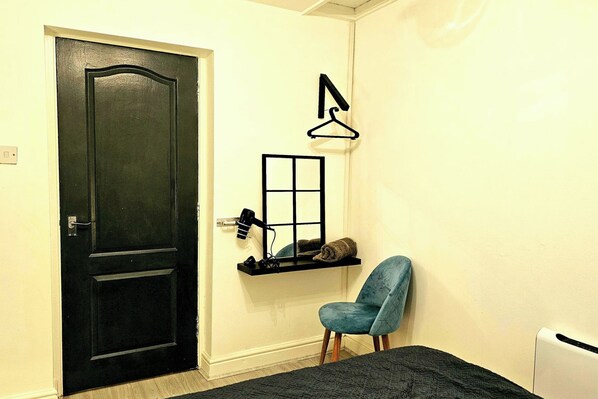 A room with a black door, a small shelf with a mirror and a towel, a blue chair, and a radiator. - Flat - Sleeps 4 - Wifi (Bridgend)