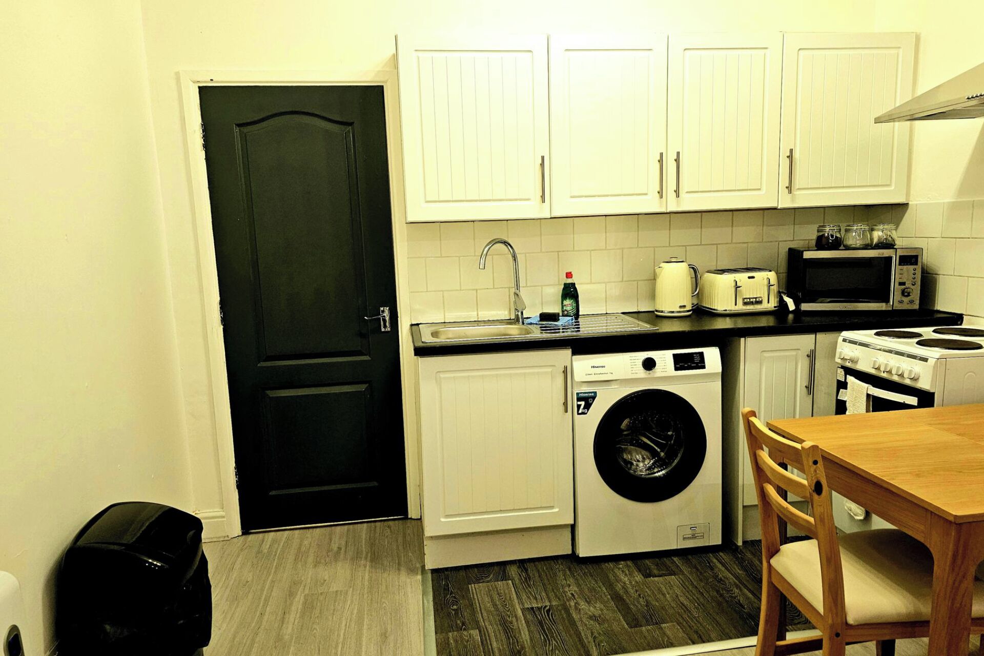 A compact kitchen with white cabinets, a washing machine, a microwave, and a toaster.