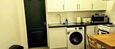 A compact kitchen with white cabinets, a washing machine, a microwave, and a toaster.