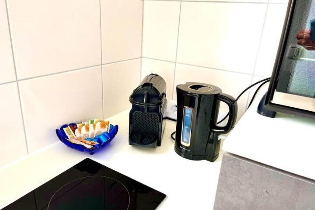 Keittiön työtasolla on kahvinkeitin, vedenkeitin ja sininen kulho, jossa on erilaisia esineitä.