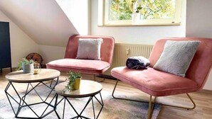 A modern living room with two pink armchairs, a round coffee table, and a small side table with a plant. - Zuhause im Ruhrgebiet 2 mit Balkon (Oberhausen)