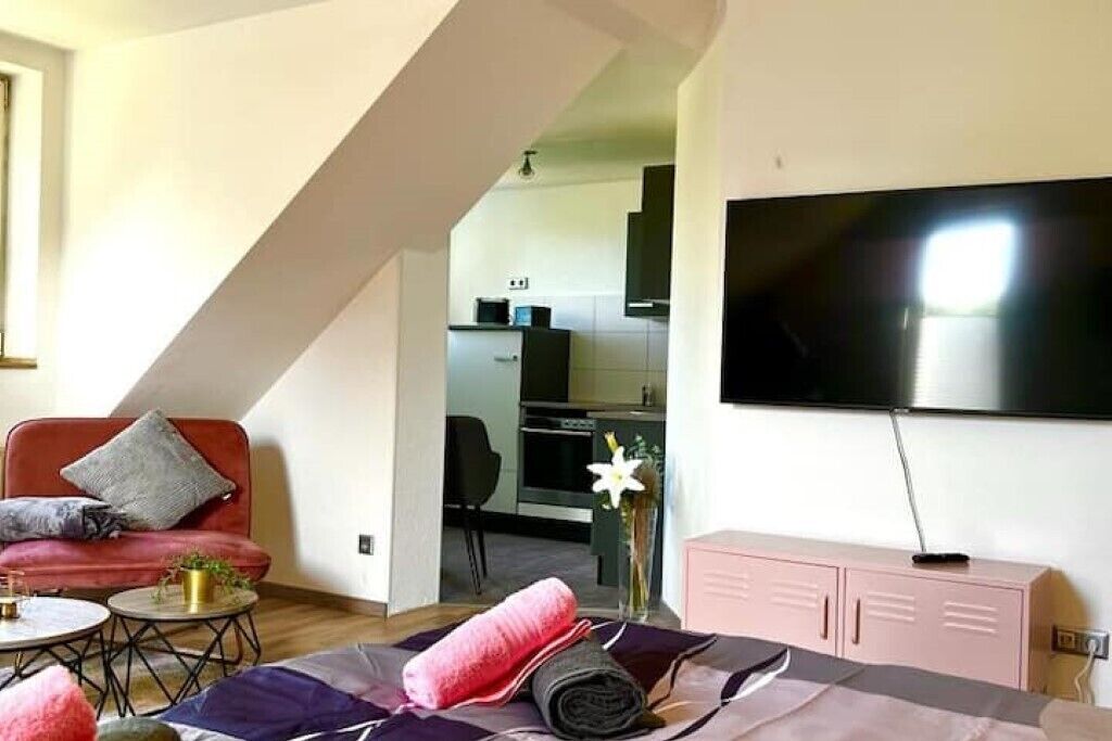 A modern living room with a sofa, a coffee table, a flat-screen TV mounted on the wall, and a staircase leading to an upper level.