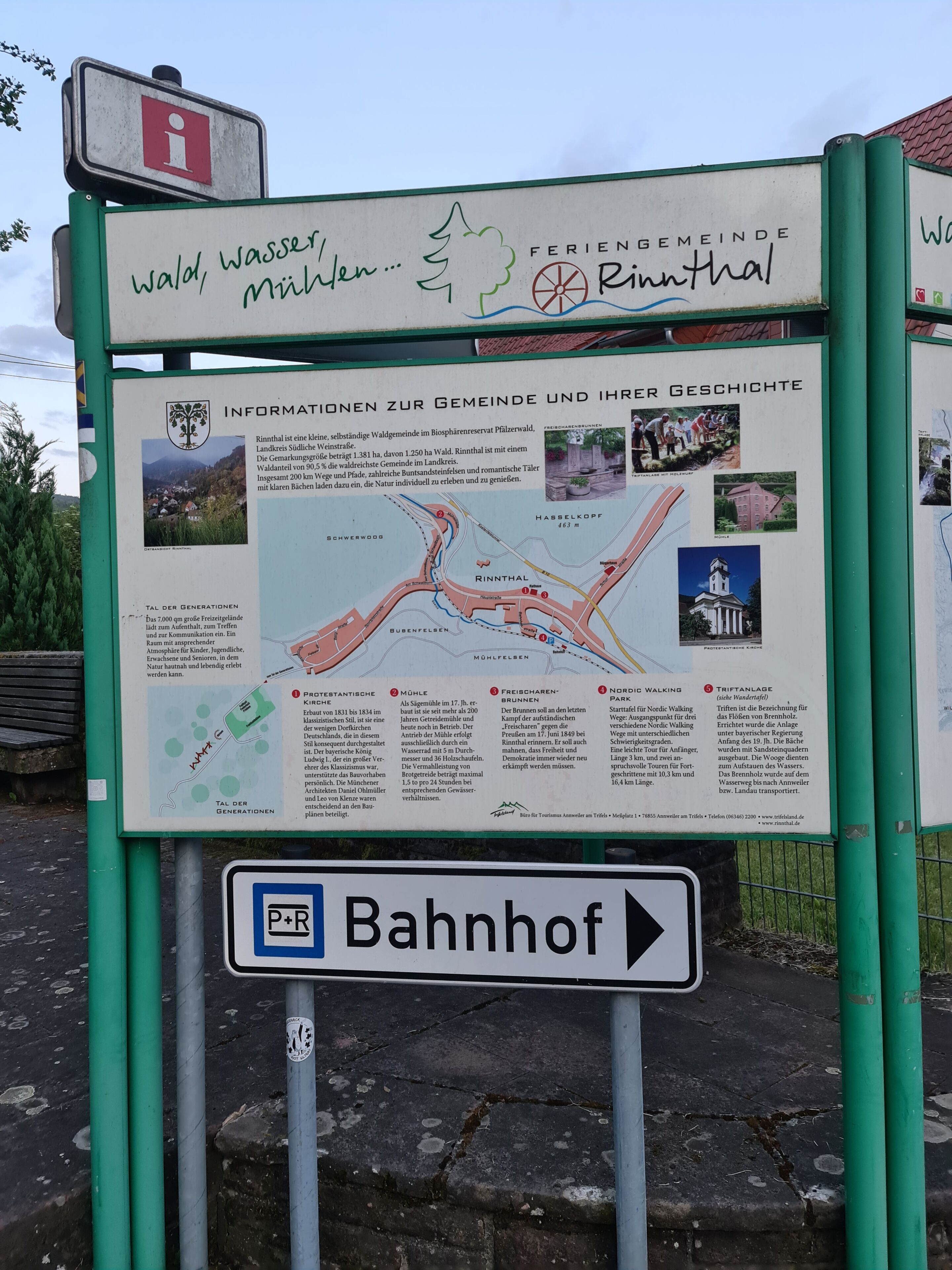 Un cartel con información sobre Rinnthal, que incluye un mapa y fotografías de lugares de interés locales.
