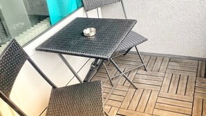 A small outdoor seating area with a metal table and two chairs, a wooden herringbone floor, and a glass balustrade. - Apartment Nähe Flughafen DUS mit Balkon (Düsseldorf)