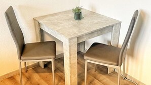 A small, square dining table with a light-colored, textured top and metal legs. There are two chairs with dark cushions and metal frames. A small potted plant is on the table. - Apartment Nähe Flughafen DUS mit Balkon (Düsseldorf)