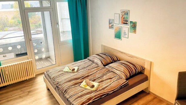 A bedroom with a bed, a radiator, a window with curtains, and wall art. - Apartment Nähe Flughafen DUS mit Balkon (Düsseldorf)