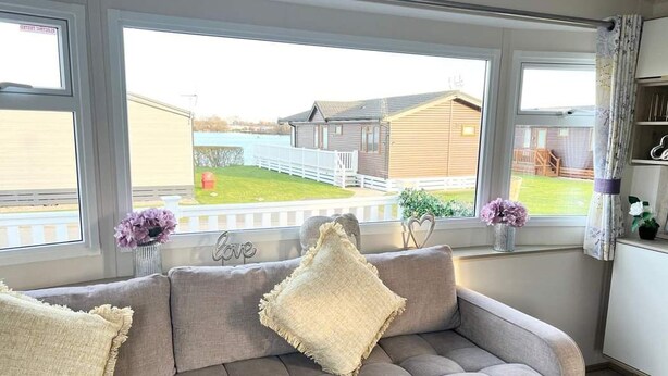 Un salón con sofá, ventanas amplias y vista a un espacio exterior cercado.