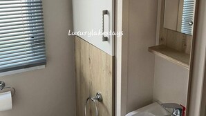 Un baño con tocador de madera, lavamanos blanco y ventana con persianas.