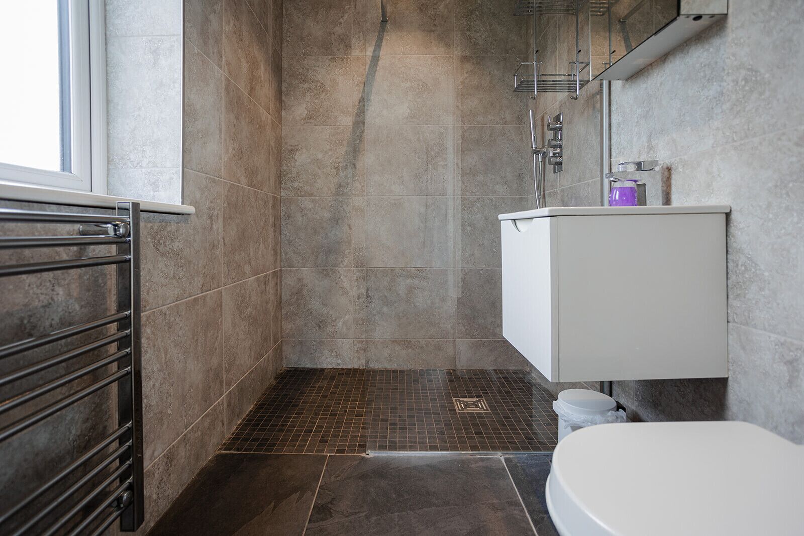 A modern bathroom with a shower, tiled walls, a toilet, and a sink with a mirror.