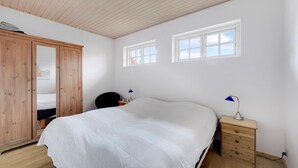 Une chambre à coucher avec un lit, une armoire en bois, deux fenêtres et une table de chevet avec une lampe.