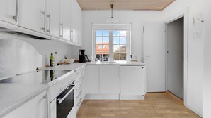 Une cuisine moderne avec des meubles blancs, un four encastré et une fenêtre donnant sur un bâtiment au toit rouge.