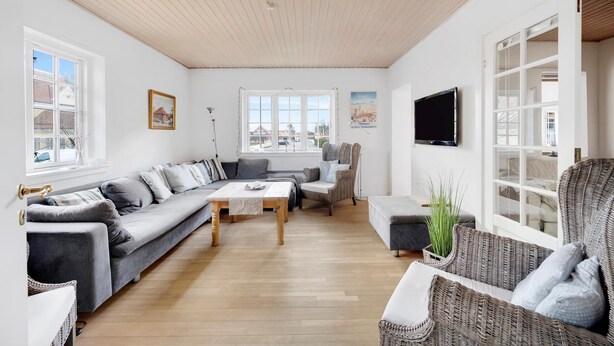 Un salon moderne avec un plafond en bois, un canapé gris, une table basse, un fauteuil en osier et un téléviseur.