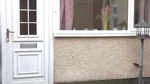 Una puerta blanca con un ventanal encima, una pared texturizada y una pequeña lámpara exterior.