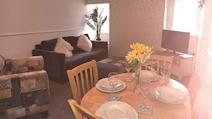Un comedor con una mesa de madera dispuesta para cuatro personas, rodeado por dos sillones y un sofá.