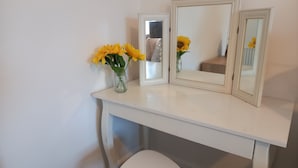 Un tocador blanco con espejo, un florero con flores amarillas y un taburete blanco.