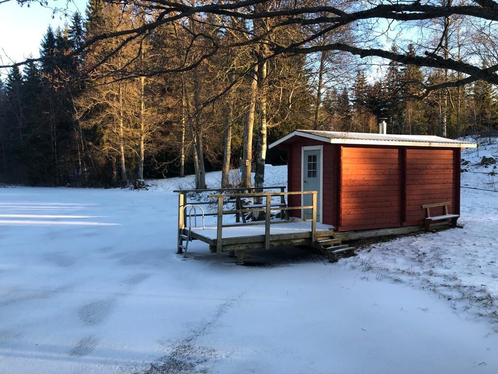 Une petite cabane en bois dotée d’une terrasse en métal et d’un banc, entourée d’un paysage enneigé et d’arbres.