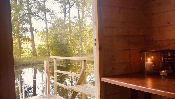 Una cabaña de madera con un muelle de madera que da a un estanque, una vela sobre la mesa y un letrero que dice 'SINGER' en la pared.