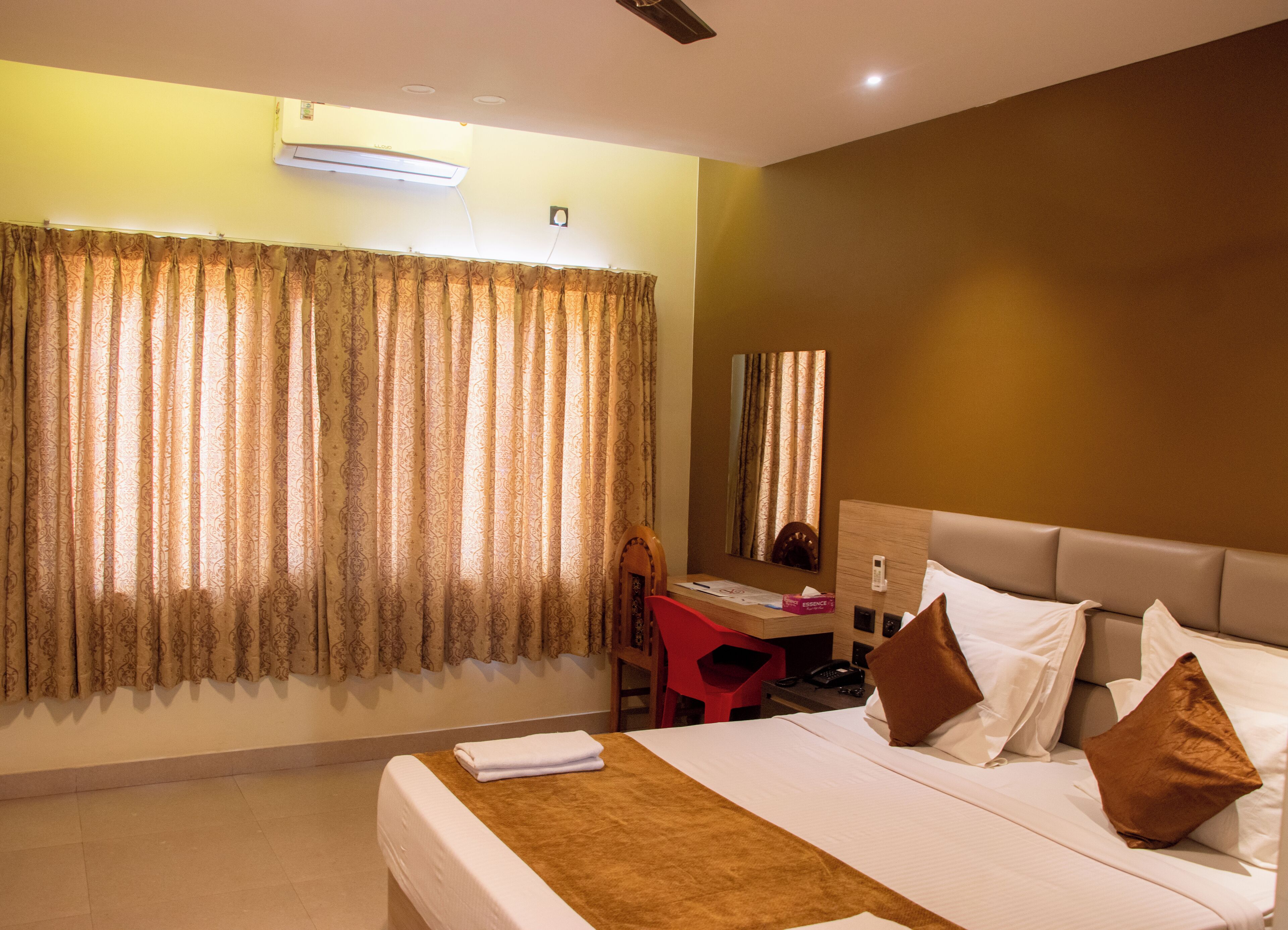 A hotel room with a bed, a desk, a chair, a mirror, and a window with curtains.
