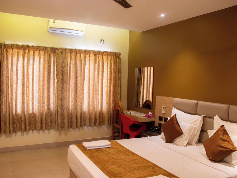 A hotel room with a bed, a desk, a chair, a mirror, and a window with curtains.