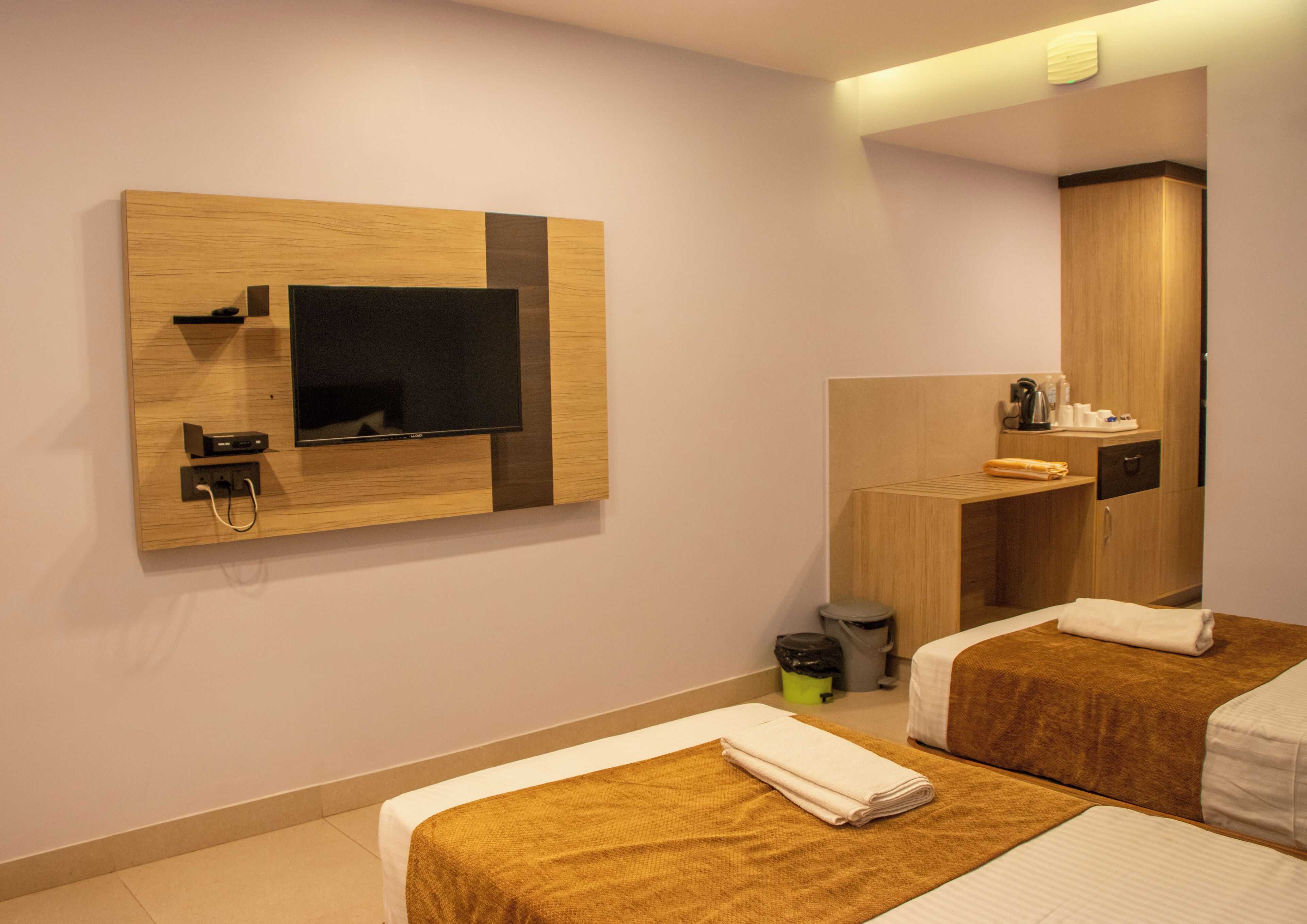 Een hotelkamer met twee bedden, een aan de muur bevestigde televisie, een spiegel en een klein kitchenette.