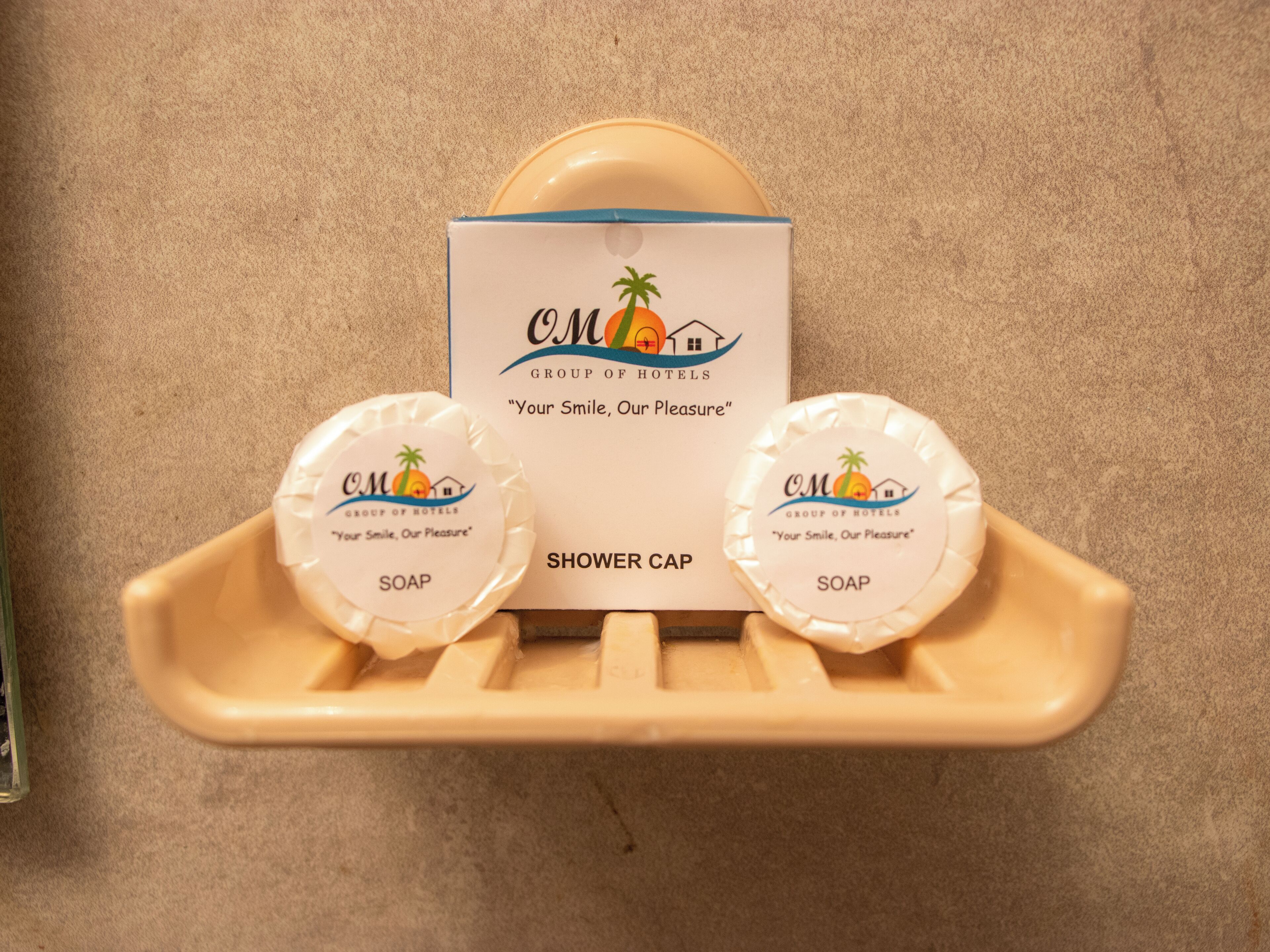 A shower cap and two soap bars on a beige tray with a sign above them.