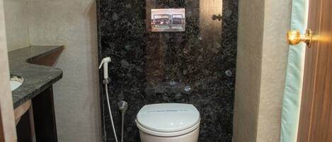 A compact bathroom with a marble wall, a white toilet, a shower, and a small sink.