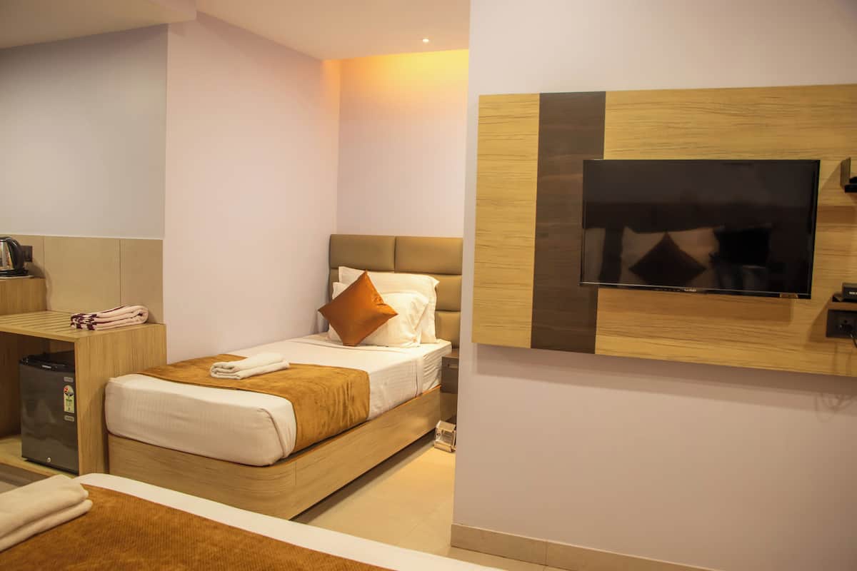 A modern hotel room with a wooden bed, a flat-screen TV mounted on the wall, and a small desk with a kettle and a trash bin.