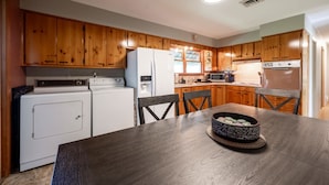A kitchen with wooden cabinets, a refrigerator, a microwave, a stove, and a dining table with chairs. - Grandma's House | Classic Indy Charm, Private Yard (Indianapolis)