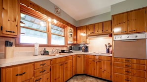 A kitchen with wooden cabinets, a microwave, a refrigerator, and a window with blinds. - Grandma's House | Classic Indy Charm, Private Yard (Indianapolis)