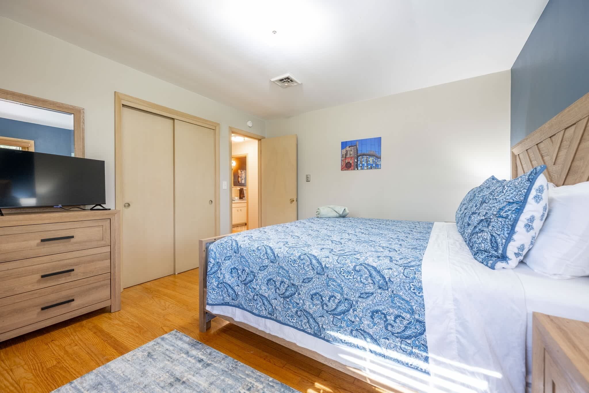 Un dormitorio con cama, cómoda, televisor y puerta que da a otra habitación.