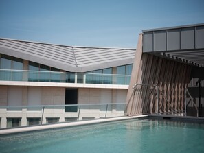 A modern building with a pool, featuring a glass facade and a sloped roof.