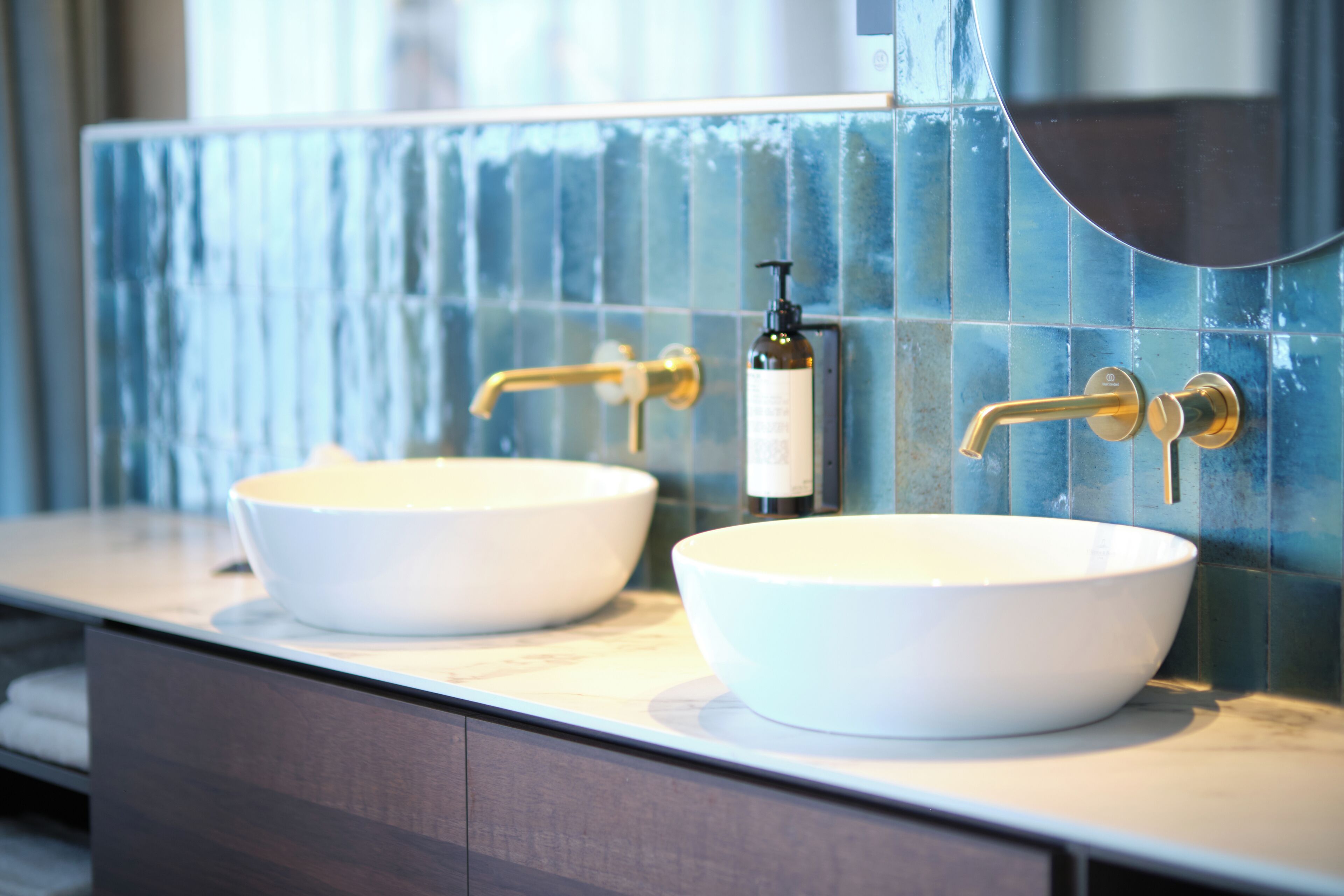 Ein Badezimmer mit zwei weißen Waschbecken, einem goldenen Wasserhahn und einer blauen Fliesenrückwand.