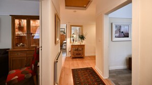A hallway with a wooden cabinet, a red chair, a small table with a lamp, and a patterned rug. - Ladyland Cottage in Maybole (Maybole)