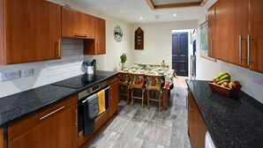 A kitchen with wooden cabinets, a black countertop, a tiled backsplash, and a dining area with a table and chairs. - Ladyland Cottage in Maybole (Maybole)