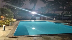 A swimming pool with a tiled deck, surrounded by palm trees and a brick wall. - GoanFiesta Beach House Calangute (Calangute)