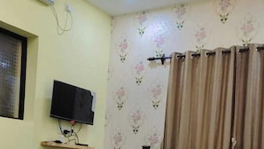 A bedroom with a bed, a television on a stand, a window with curtains, and a ceiling fan. - GoanFiesta Beach House Calangute (Calangute)