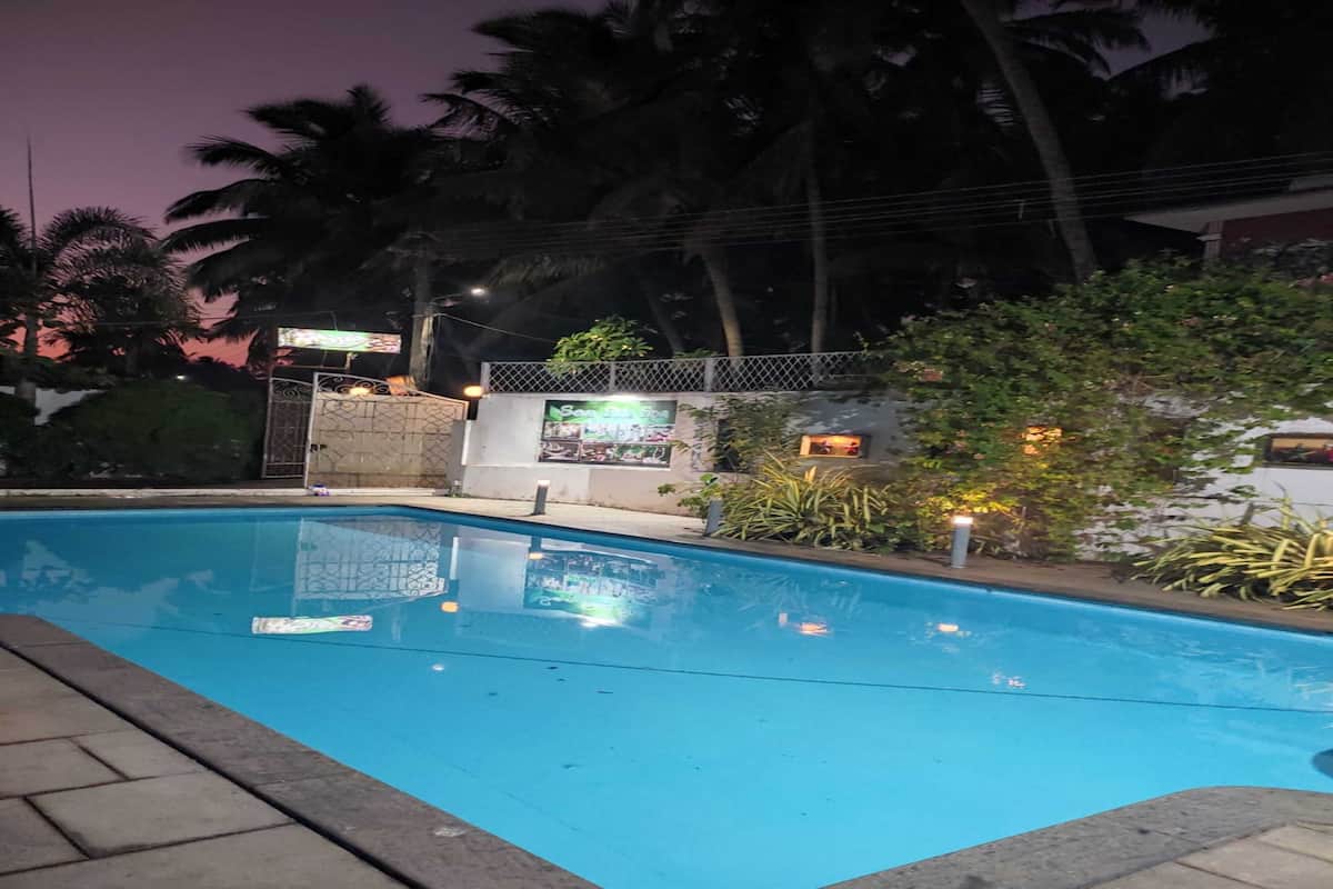 A swimming pool with a tiled edge, surrounded by palm trees and a fence.
