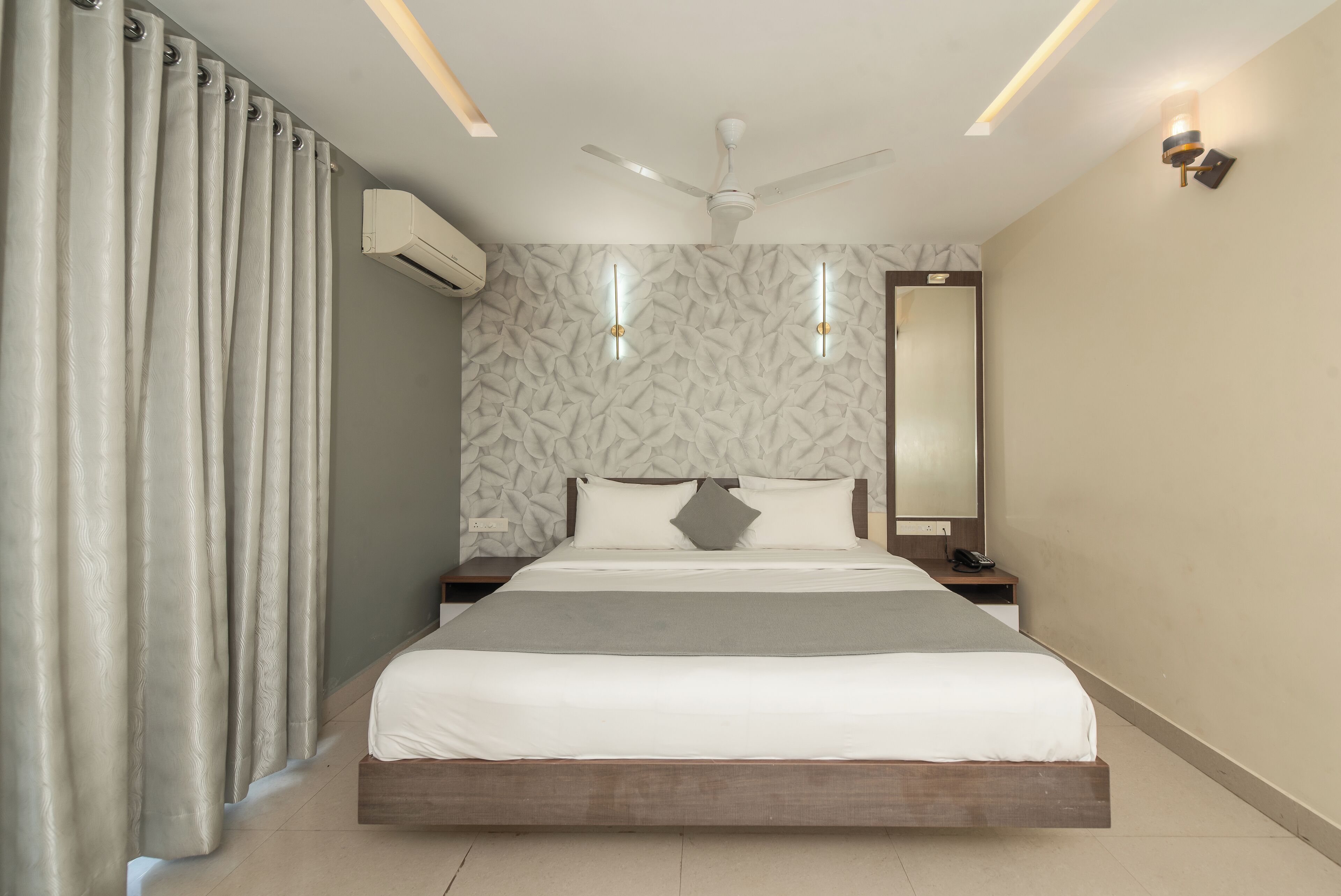 Une chambre moderne comprenant un lit, un ventilateur de plafond, un appareil de climatisation, une table de chevet et un miroir.
