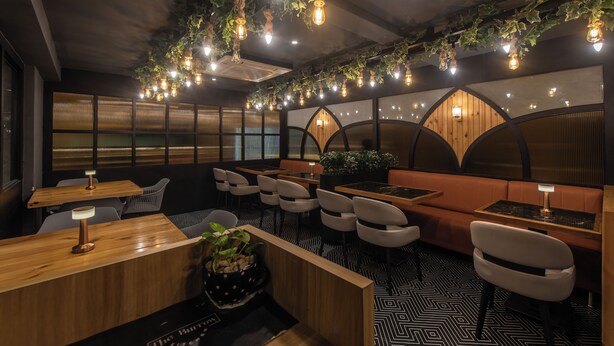 A restaurant interior with wooden tables, cushioned seating, hanging light fixtures, and a patterned floor. - Hotel Shoolin Grand (Mangaluru)