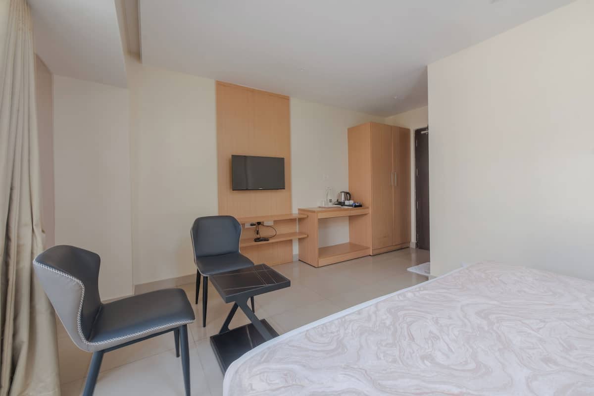 A hotel room with a bed, two chairs, a desk with a flat-screen TV, a coffee machine, and a wardrobe.