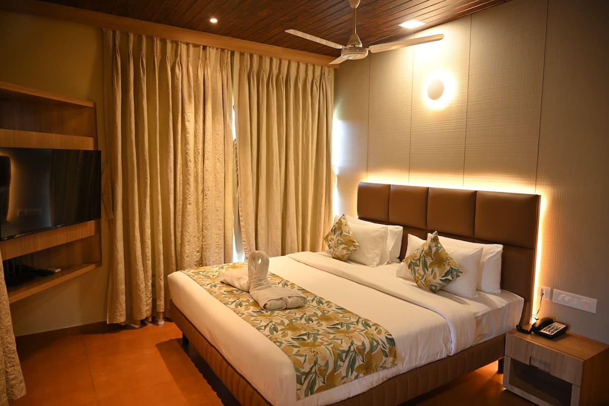 A hotel room with a bed, a TV on a shelf, a bedside table with a phone, and a ceiling fan.