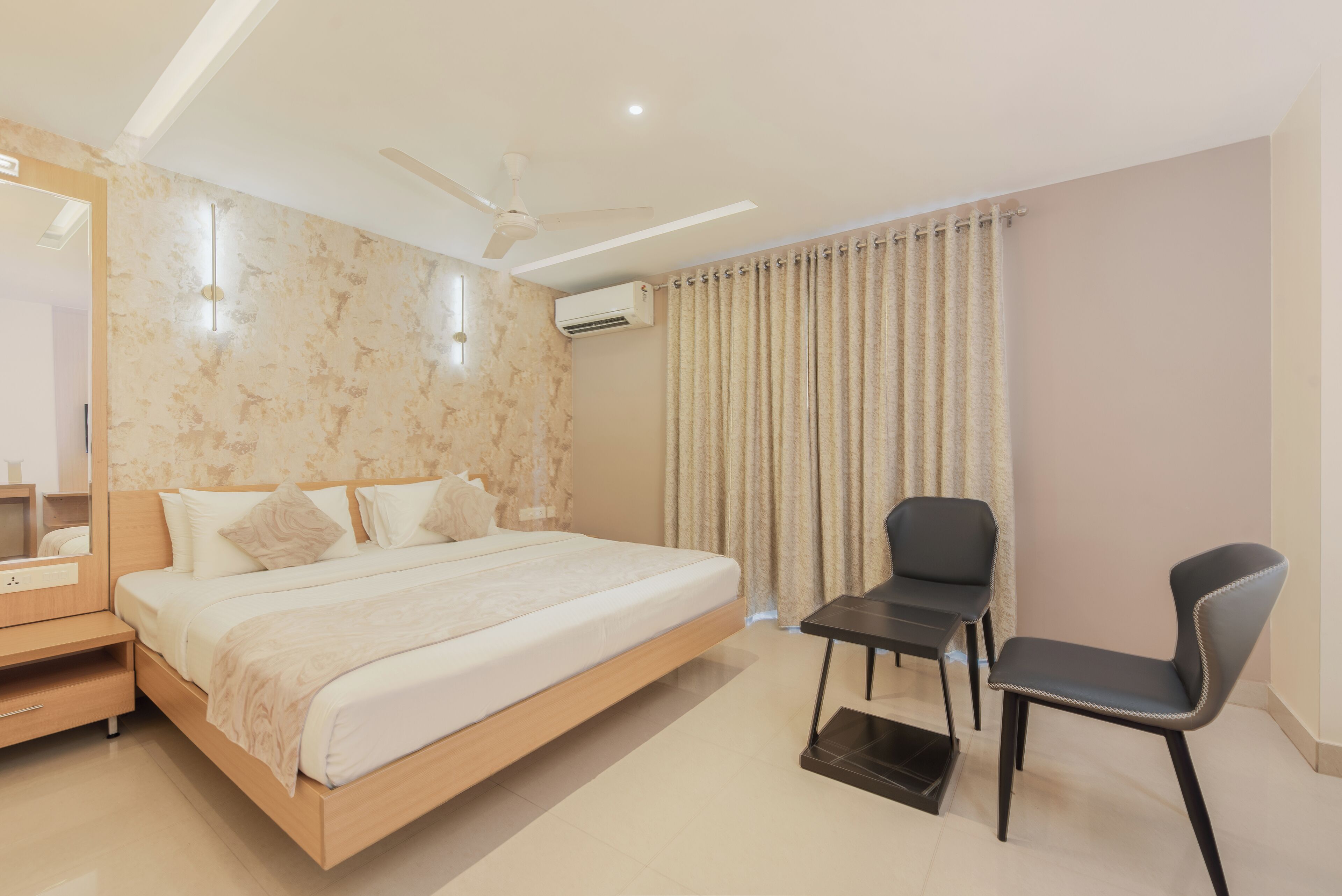 Habitació d'hotel moderna amb un llit de fusta, un escriptori amb cadira, un ventilador de sostre i una finestra amb cortines.