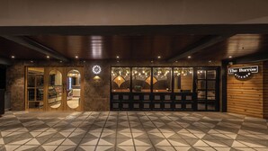 A hotel lobby with a geometric patterned floor, wooden paneling on the walls, and a sign for 'The Burrow Kitchen'. - Hotel Shoolin Grand (Mangaluru)