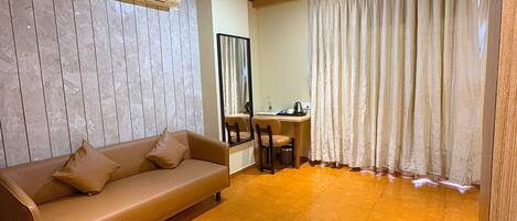 Una habitación con techo de madera, un sofá color beige con almohadas, una pequeña mesa con sillas y un gran ventanal con cortinas.