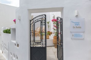 A white building with a black gate, potted plants, and a sign with contact information. - Ep Avlis Apartments (Naxos)