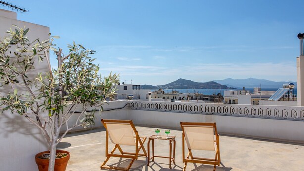 A rooftop terrace with two wooden chairs and a small table, a potted plant, and a view of the sea and mountains. - Ep Avlis Apartments (Naxos)