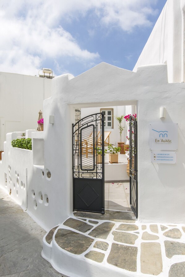 A white building with a black gate, a stone pathway, and a sign with contact information. - Ep Avlis Apartments (Naxos)
