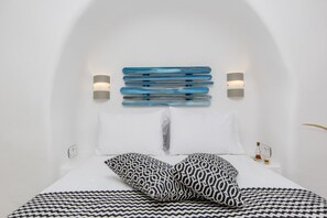 A modern bedroom with a white wall, a bed with patterned bedding, and a unique blue and white headboard. - Ep Avlis Apartments (Naxos)