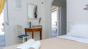 A hotel room with a bed, a chair, a small table with a lamp, a mirror, and a view of the outside. - Ep Avlis Apartments (Naxos)